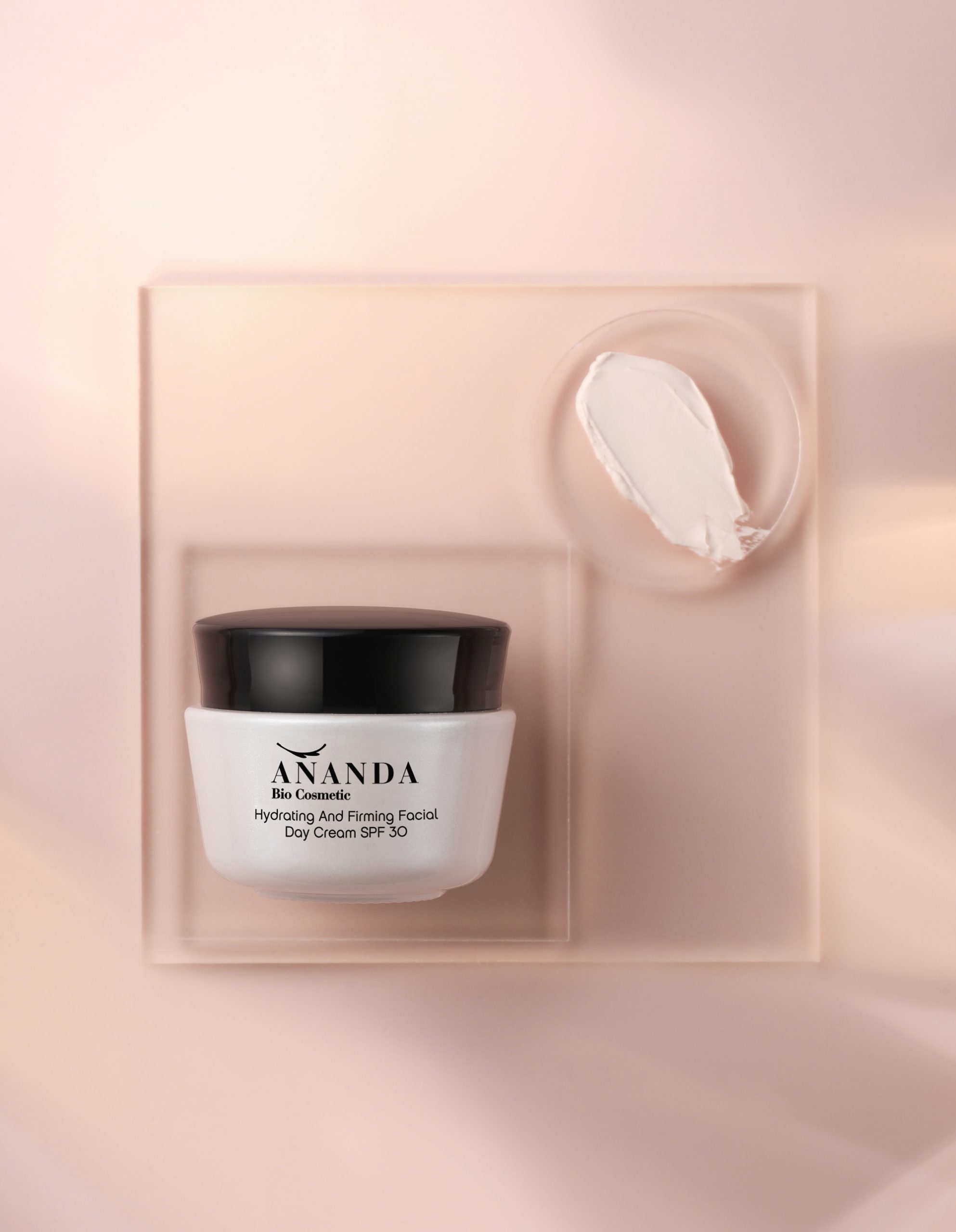 Jar of 'ANANDA Bio Cosmetic Hydrating And Firming Facial Day Cream SPF 30' on a blush-pink backdrop, with a sample smear of the cream on a matching palette above